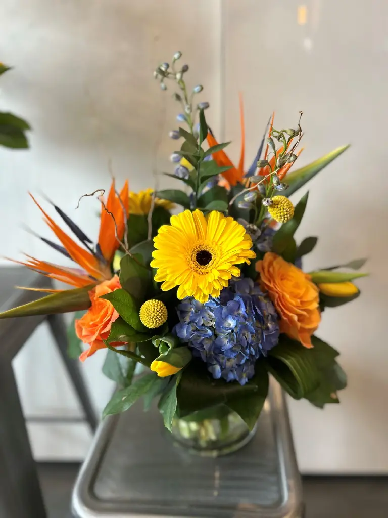 Hommage lumineux – accompagnement d’urne composé de deux arrangements floraux en vase orange, jaune et bleu à Montréal.1.webp