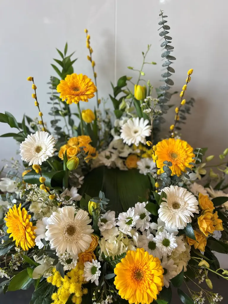 Douce lumière – accompagnement d’urne jaune et blanc avec gerberas, roses, tulipes et feuillage à Montréal.1.webp