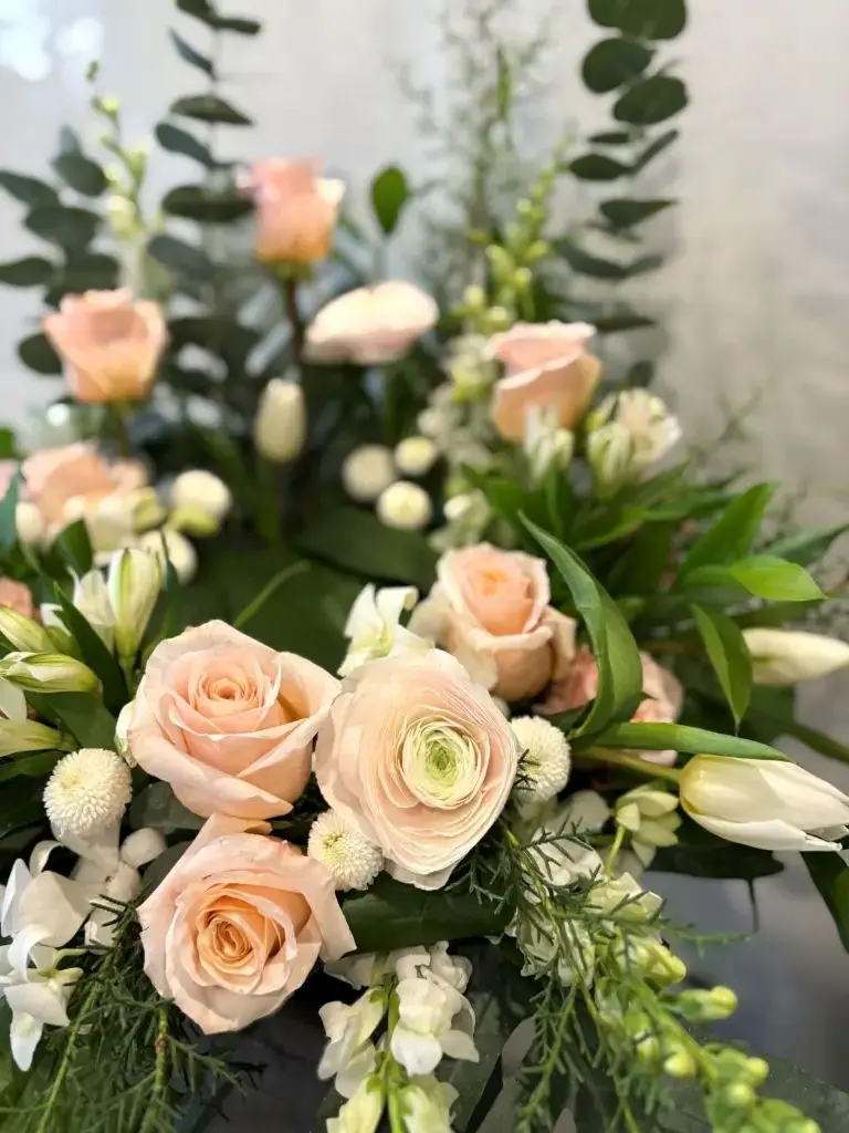 Douce présence – accompagnement d’urne rose pêche, blanc et vert avec roses, renoncules, tulipes et feuillage à Montréal.1.webp