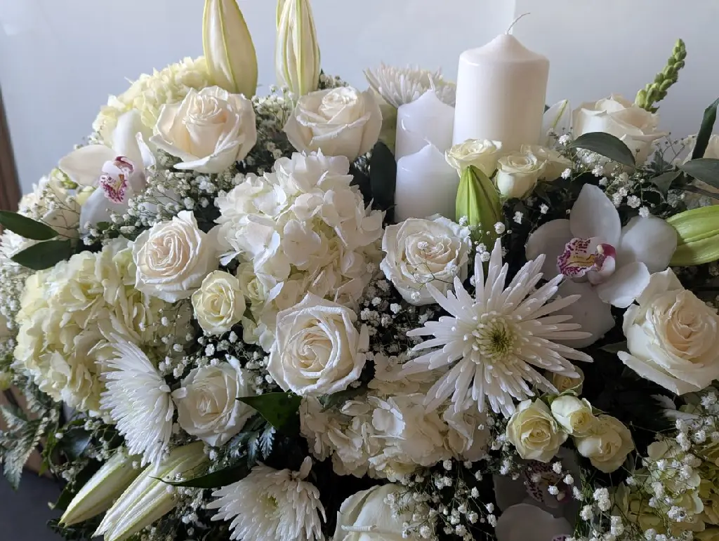 Dans la lumière – coussin de cercueil blanc avec bougies, roses, orchidées Phalaenopsis, hydrangées et feuillage à Montréal.1.webp