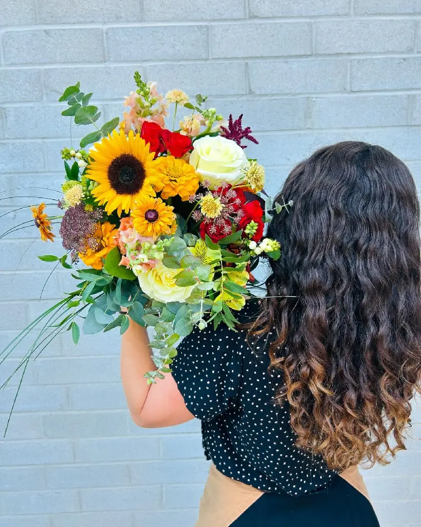 Bouquet coloré aux tons chauds avec roses rouges et blanches, fleurs jaunes, orange et pêche et eucalyptus, créé par La Maison d’Alcantara à Montréal, livraison.webp